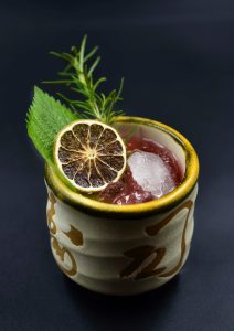 Elegant cocktail with herbs and dehydrated lime slice in a decorative cup.
