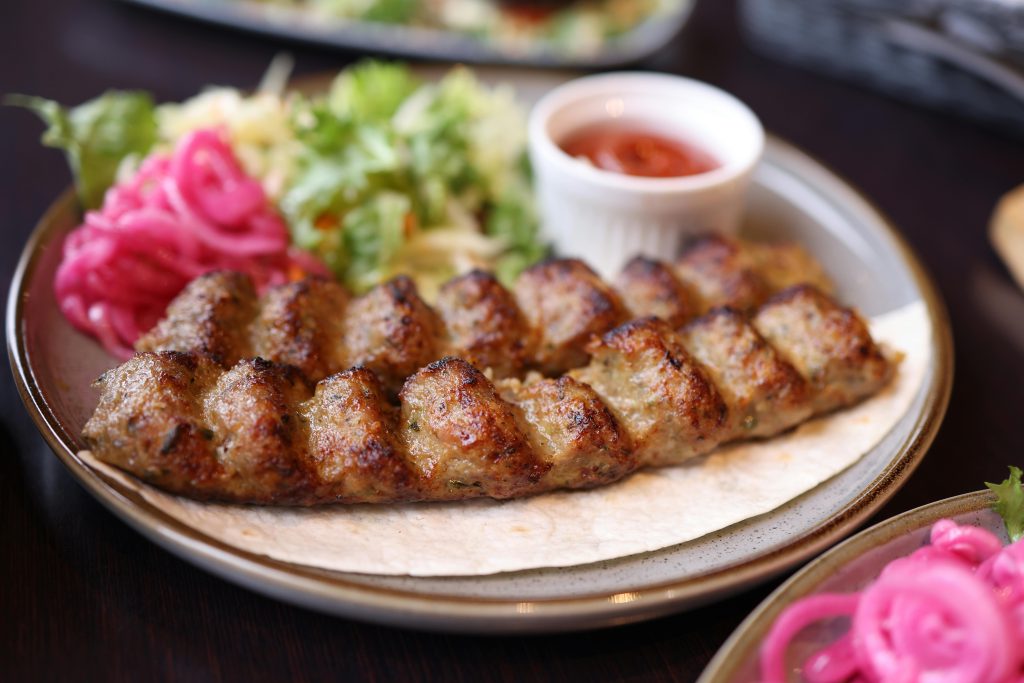 A plate of succulent grilled kebab served with fresh salad and sauce, perfect for food lovers.